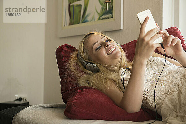 Schöne junge Frau hört Musik und entspannt auf dem Sofa im Wohnzimmer  München  Bayern  Deutschland