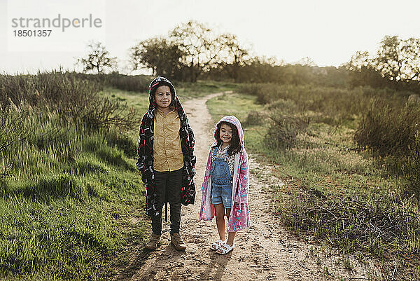 Junge und junges Mädchen im schulpflichtigen Alter tragen Roben auf einem Feld mit Hintergrundbeleuchtung