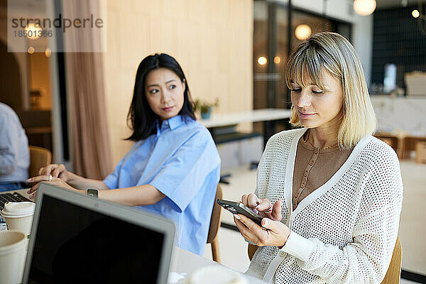 Geschäftsfrau sitzt mit Kollegin im Café und nutzt Smartphone