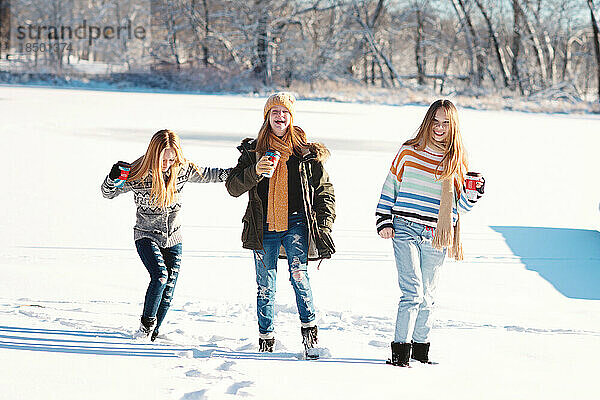 Drei kleine Mädchen spielen an einem Wintertag im Schnee auf einem zugefrorenen See.