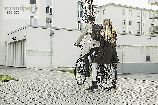 Rückansicht eines jungen Paares  das auf der Straße Fahrrad fährt  München  Bayern  Deutschland