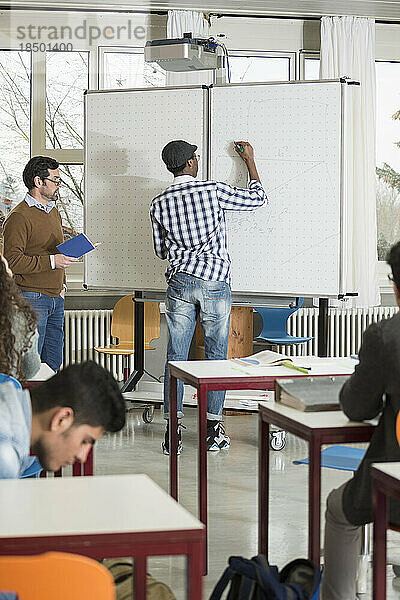 Schüler schreibt auf Whiteboard und Lehrer beobachtet ihn. Schule  Bayern  Deutschland