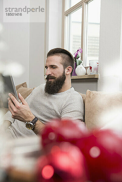 Junger Mann sitzt auf dem Sofa und benutzt ein digitales Tablet