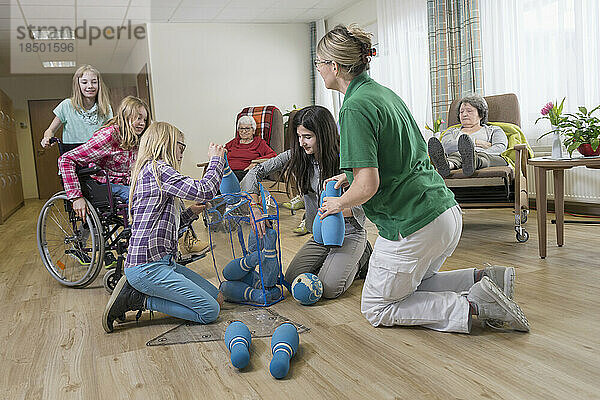 Mädchen spielen Bowling mit Krankenschwester und älteren Frauen im Pflegeheim