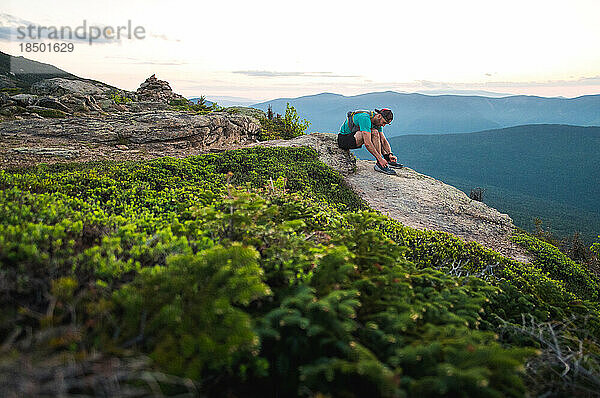 Trailrunner-Mann bindet Schuhe mit Bergen hinter sich bei Sonnenaufgang