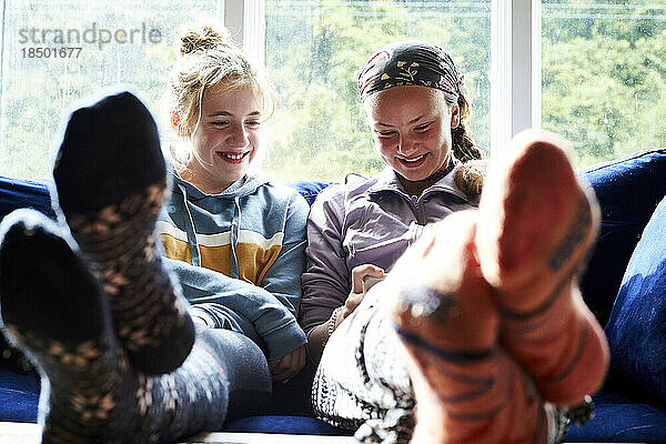 Junge Mädchen sitzen auf einer Couch  schauen auf einen Bildschirm und lachen