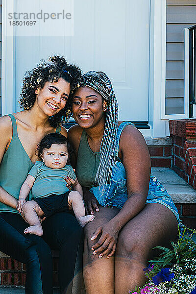 Porträt glücklicher lesbischer Mütter und süßer Söhne  die vor dem Haus sitzen