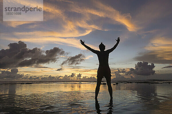 Silhouette eines Mannes mit ausgestreckten Armen bei Sonnenuntergang über dem Meer  Uluwatu  Bali  Indonesien