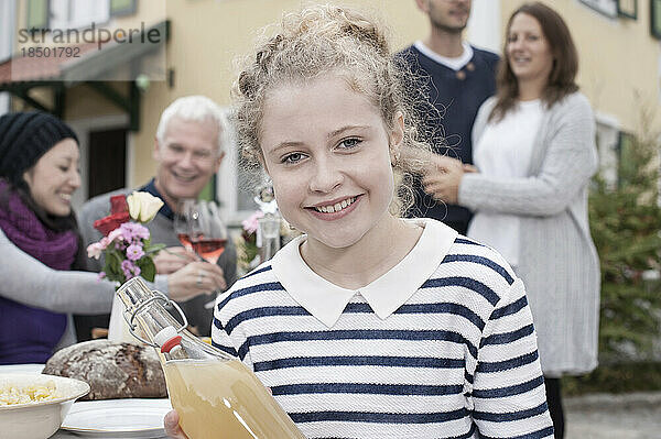 Porträt eines Teenager-Mädchens  das Apfelsaft in der Hand hält und mit der Familie im Hintergrund lächelt  Bayern  Deutschland