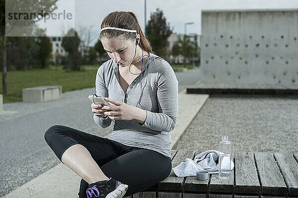 Junge Frau macht nach dem Training eine Pause und überprüft die Sporttestergebnisse auf dem Handy  Bayern  Deutschland