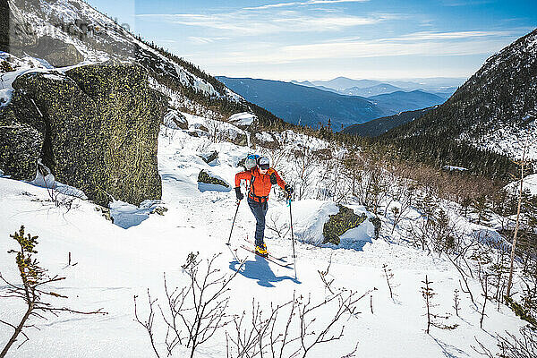 Mann fährt im Schnee bergauf  umgeben von Felsen und Bergen