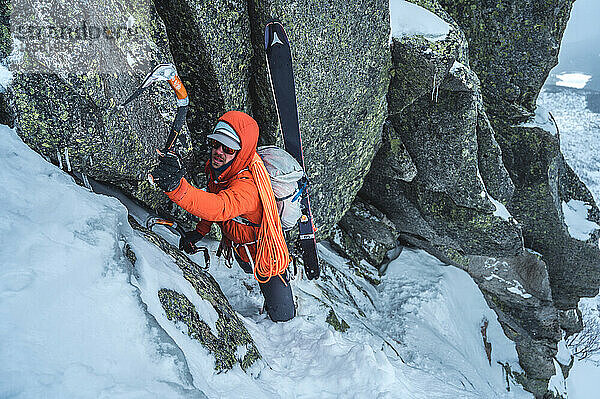 Mann klettert beim Skibergsteigen mit Skiern auf Fels und Eis