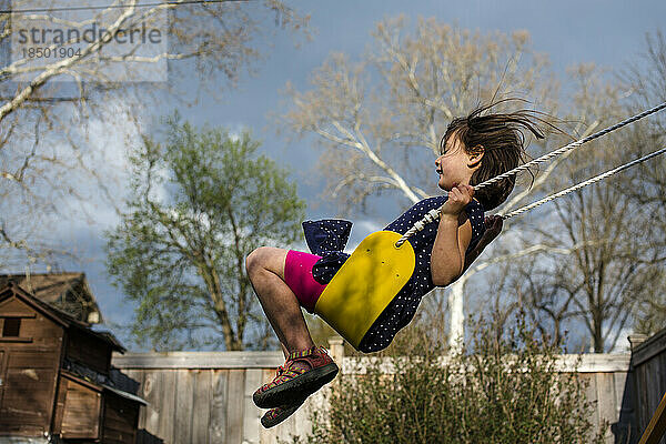 Ein glückliches Mädchen auf einer gelben Schaukel an einem windigen  stürmischen Frühlingstag