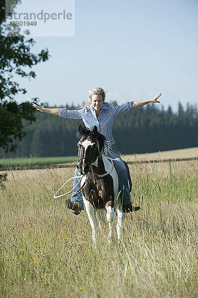 Mitte erwachsene Frau reitet galoppierendes Pferd ohne Zügel auf dem Bauernhof  Bayern  Deutschland