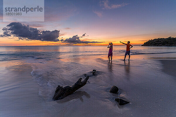 Mann und Frau bewundern den Sonnenuntergang am tropischen Strand in der Karibik