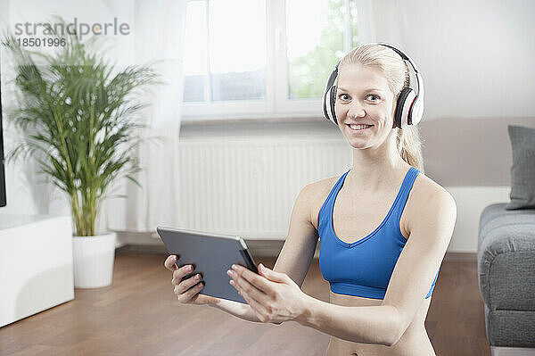 Porträt einer jungen Frau  die im Wohnzimmer ein digitales Tablet nutzt und Musik hört  Bayern  Deutschland