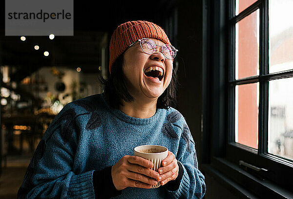 Asiatische Frau lacht beim Kaffeetrinken in einem Café