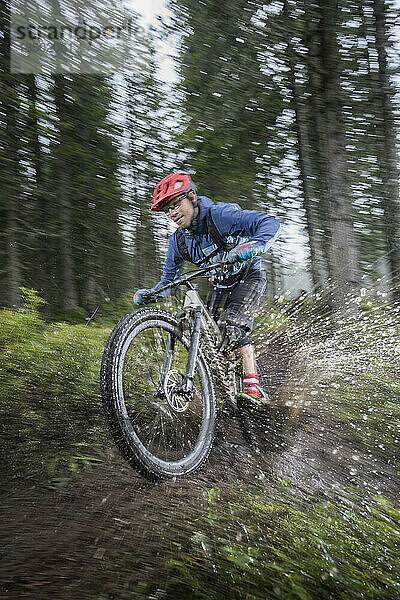 Mountainbiker fährt an einem regnerischen Tag durch eine Pfütze im Wald  Saalfelden  Tirol  Österreich