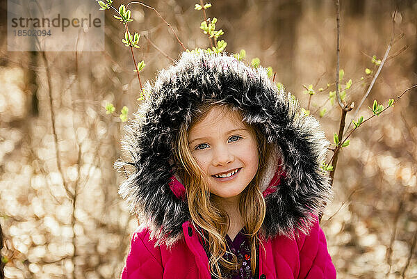 Lächelndes Mädchen blickt mit Fellkapuze auf dem Kopf im Herbstwald in die Kamera