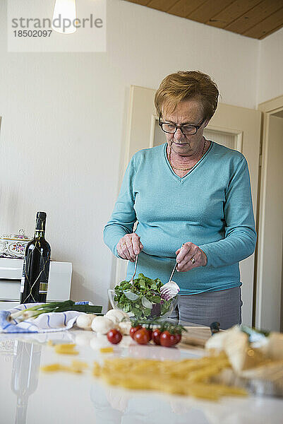 Alte Frau mischt Salat auf dem Küchentisch