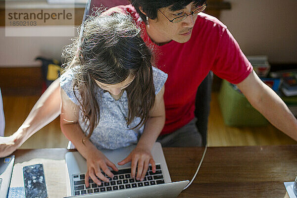 Oben: Mädchen  das auf dem Schoß seines Vaters vor dem Computer sitzt