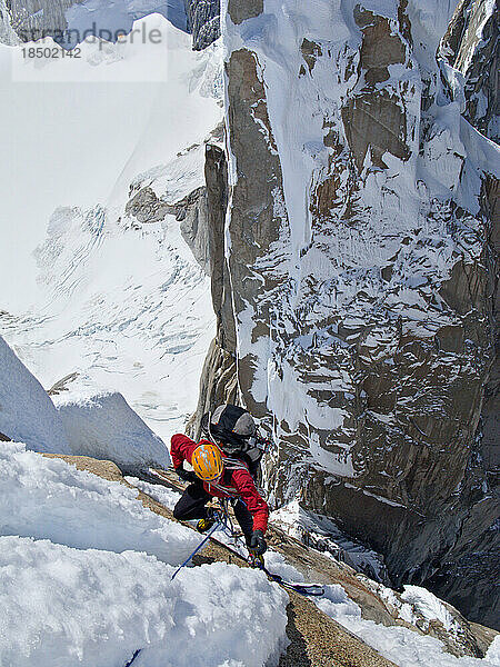 Ein Alpinist klettert an der steilen Nordwand des Cerro Torre vorbei an Schnee und Eis.