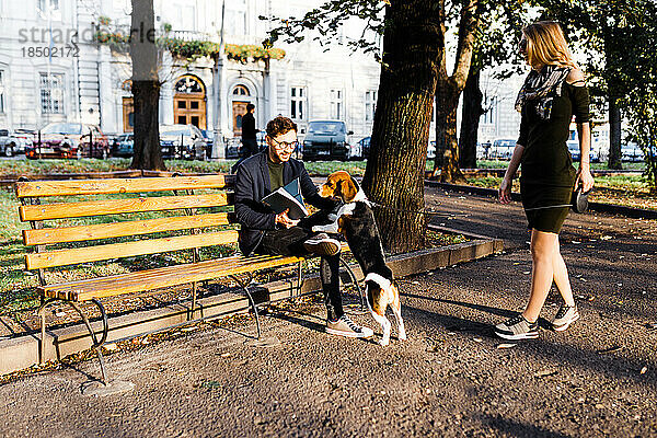 Mann mit Beagle begrüßt eine junge Blondine im Park