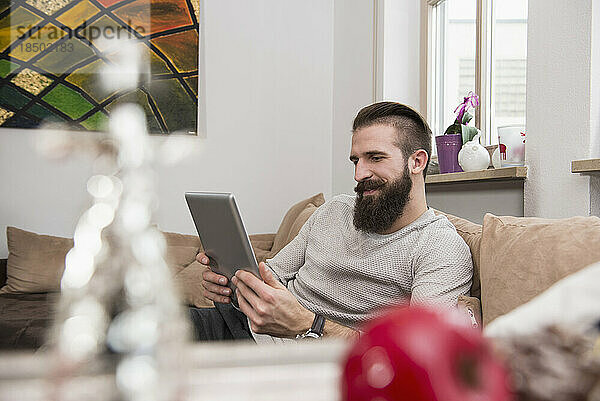 Junger Mann nutzt digitales Tablet und entspannt auf dem Sofa