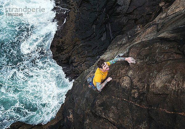 Mann klettert auf einer Klippe am Meer  darunter krachen die Wellen