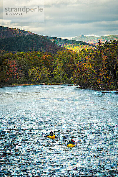 Zwei Paddler fahren mit Herbstlaub flussabwärts