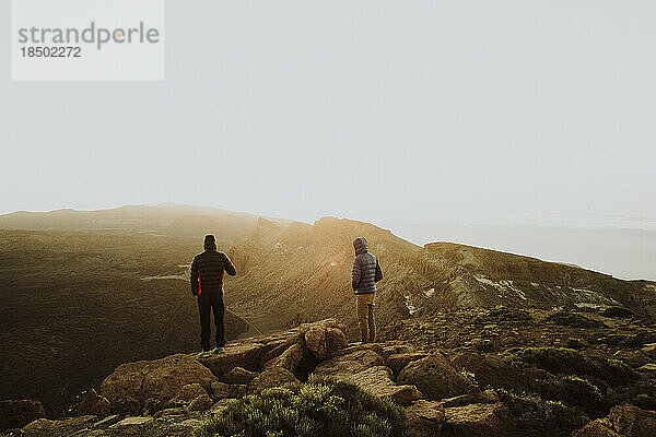 Zwei Männer stehen auf einem Berggipfel und beobachten den Sonnenaufgang