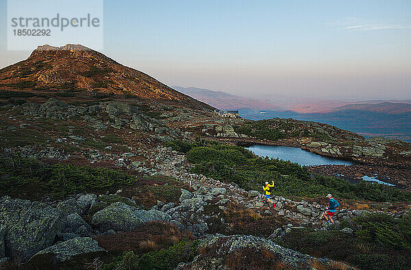 Männliche Trailrunner laufen bei Sonnenaufgang in den Bergen über Felsen