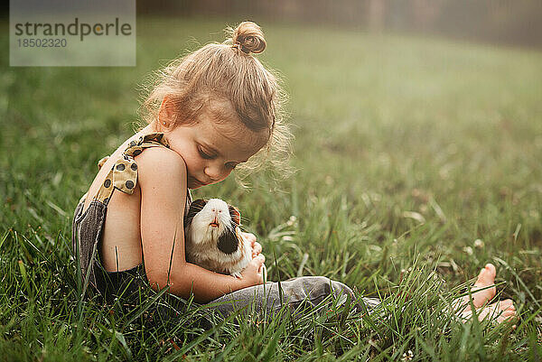 Kleines Mädchen kuschelt ihr Meerschweinchen im Gras