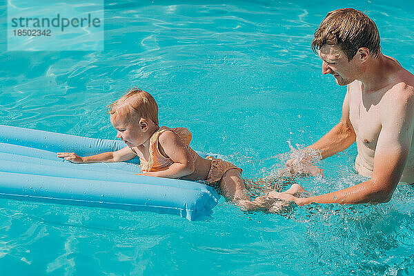 Vater und kleine Tochter schwimmen draußen auf einer aufblasbaren Matratze