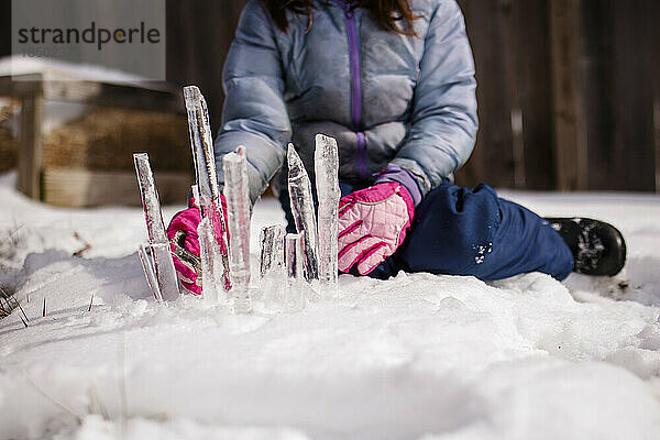 Nahaufnahme eines Kindes  das mit Eiszapfen eine Skulptur im Schnee herstellt