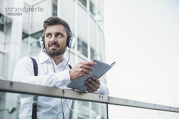 Geschäftsmann hört Musik mit Kopfhörern auf einem digitalen Tablet  München  Bayern  Deutschland