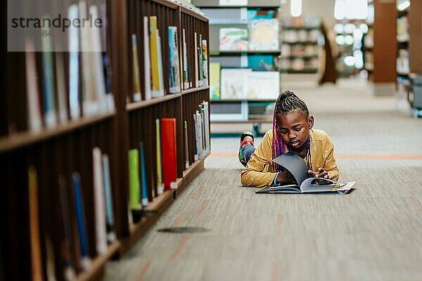 Junges schwarzes Mädchen liest Bibliotheksbuch