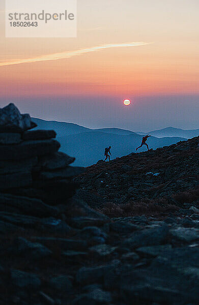 Silhouette männlicher Trailrunner  die bei Sonnenaufgang den Bergrücken hinauflaufen