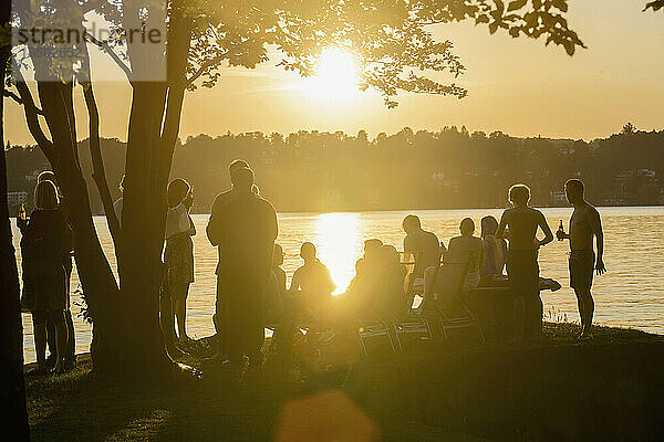 Gruppe junger Freunde feiert bei Sonnenuntergang am Seeufer  Bayern  Deutschland