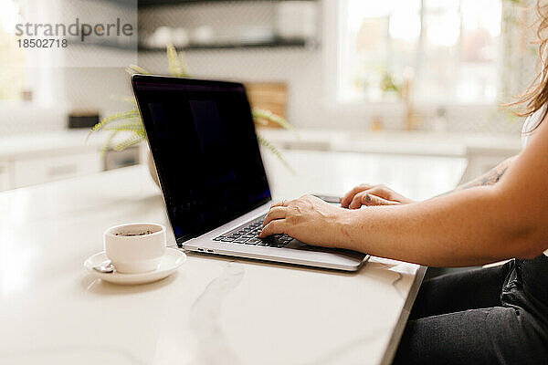 Seitenansicht einer Frau  die mit Kaffee drinnen am Computer arbeitet