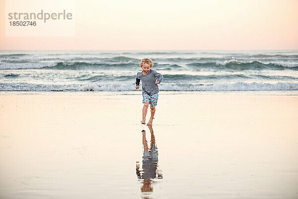 Glücklicher kleiner Junge  der am Strand läuft
