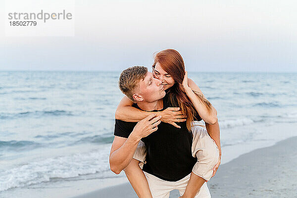 Glückliche Liebende haben Spaß und albern am Strand am Meer herum