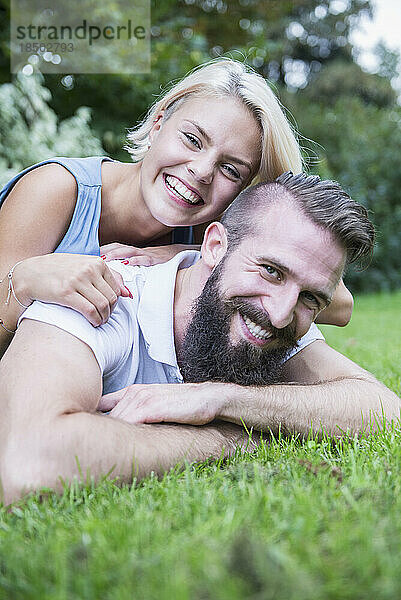 Porträt eines glücklichen jungen Paares  das im Garten liegt  Bayern  Deutschland