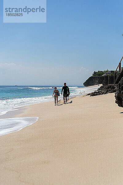 Junges Surferpaar mit Surfbrettern spaziert am Meer entlang.