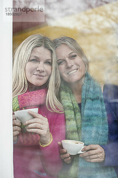 Zwei Freunde schauen durchs Fenster und trinken Kaffee in einem Café  Bayern  Deutschland