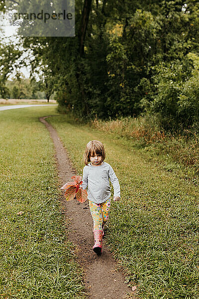 Junges Mädchen  das auf einem Feldweg läuft und rote Blätter in der Hand hält