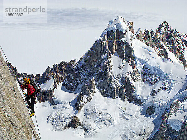 Ein Kletterer erklimmt die steile Nordwand des Torre Egger mit den Gipfeln des Cerro Rincon und den Gletschern Südpatagoniens