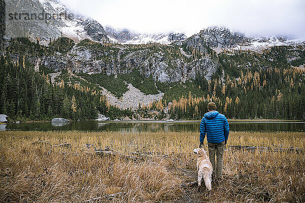 Mann kratzt Hund am Kopf  während er die Aussicht auf die Alpen genießt