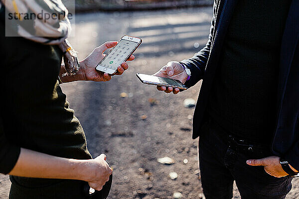 Ein Mann und eine junge Blondine tauschen im Park Telefone aus