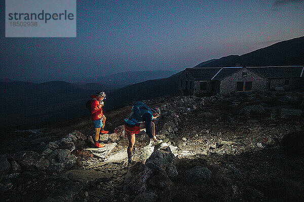 Männliche Trailrunner binden im Morgengrauen in den Bergen mit Stirnlampen Schuhe